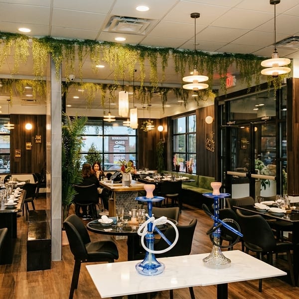 Modern restaurant interior with dark wood walls, green velvet banquettes, hanging plants, and elegant lighting.