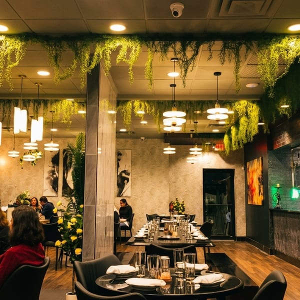 A modern restaurant interior with hanging greenery, warm lighting, diners, and an open kitchen.