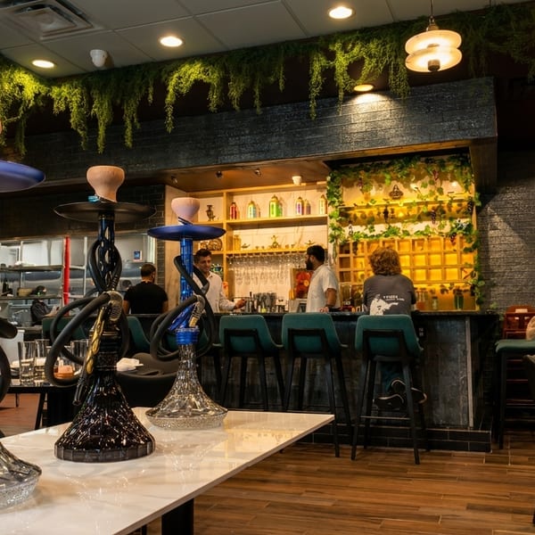 Interior of a restaurant with hookahs on a table, a bar with patrons, and hanging greenery.
